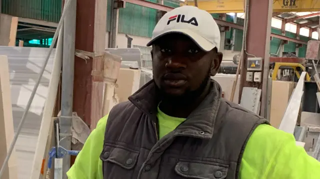 Le travailleur migrant Makan, originaire du Mali, regarde la caméra dans son uniforme de travail dans l'entreprise espagnole où il travaille