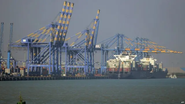 Cargo ship at the port of Mundra, next to several large metal cranes.