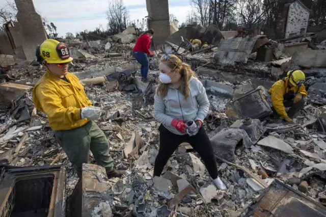 Unos bomberos ayudan a una mujer a examinar los restos de su casa destruida por el incendio en el área de Pacific Palisades de Los Ángeles, California, EE. UU., el 22 de enero de 2025. 