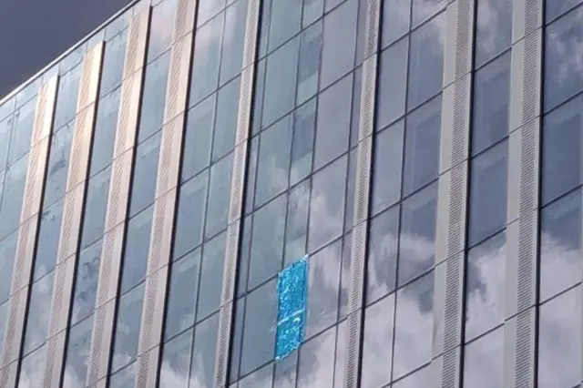 La parte superior de Britannia Point, un gran bloque de pisos con numerosas ventanas a lo largo de su fachada. Una cubierta azul cubre el espacio donde se desprendió un panel de la ventana.