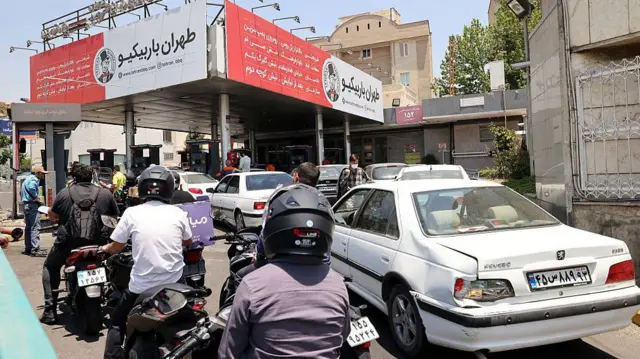 رانندگان خودرو در ۱۵ ژوئن ۲۰۲۵ پس از حملات شبانه موشکی اسرائیل که دو مخزن سوخت در تهران را هدف قرار داد، در یک پمپ‌بنزین در تهران صف کشیده‌اند.