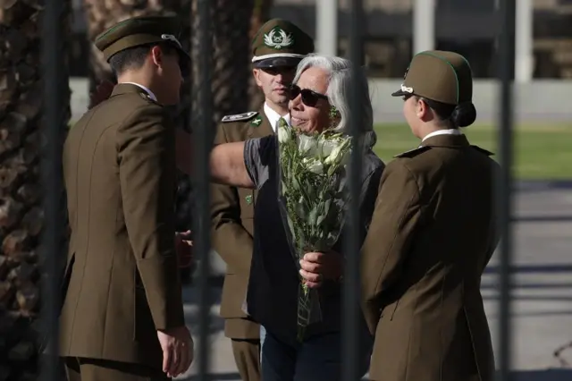 Una mujer con flores blancas saluda a unos carabineros