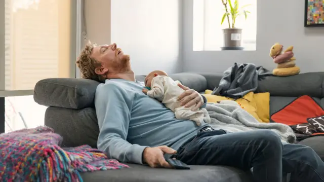 رجل منهك وعلى صدره طفل نائم