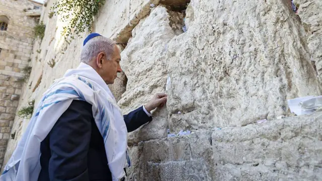 رئيس الوزراء الإسرائيلي، بنيامين نتنياهو، أمام حائط البراق/المبكى في القدس في 12 يونيو/حزيران 2025، يضع ورقة  مكتوب عليها آية من الكتاب المقدس "هو ذا شعب يقوم كلبؤة، ويرتفع كأسد" (سفر العدد 24:23)

