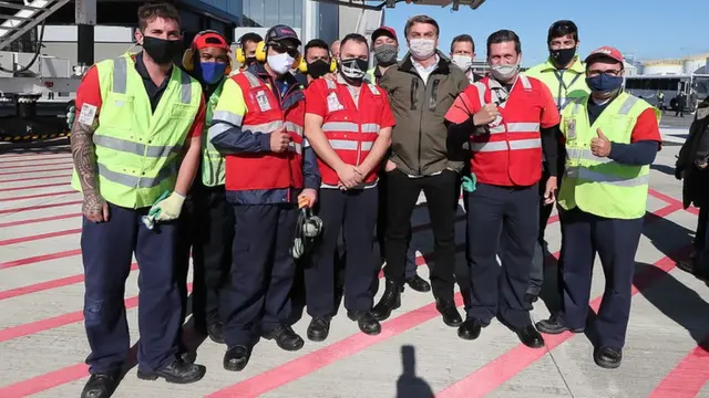 De máscara, presidente posa para foto rodeado por operadoresvoopátiodecolagem