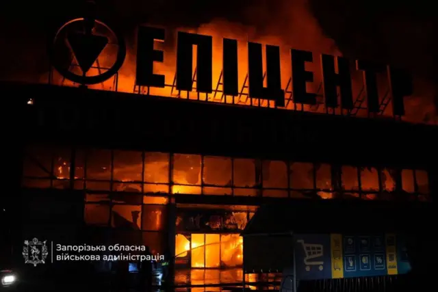 Будівля торговельного центру «Епіцентр», охоплена масштабною пожежею в нічний час. З вікон і даху вириваються полум’я та густий дим, фасад зазнав значних пошкоджень.
