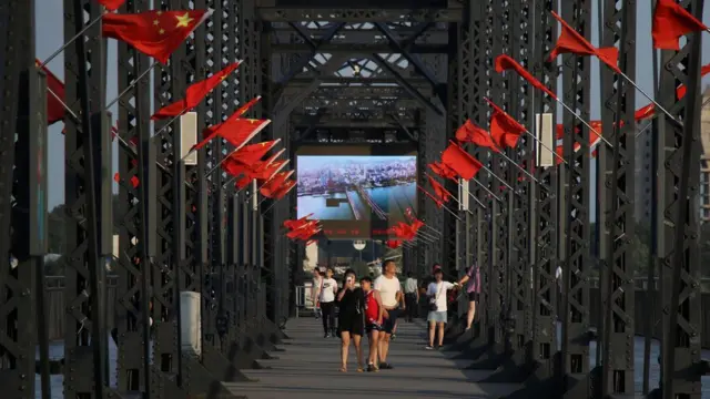 Tourists walk on the Broken Bridge over the Yalu river that divides North Korea and China