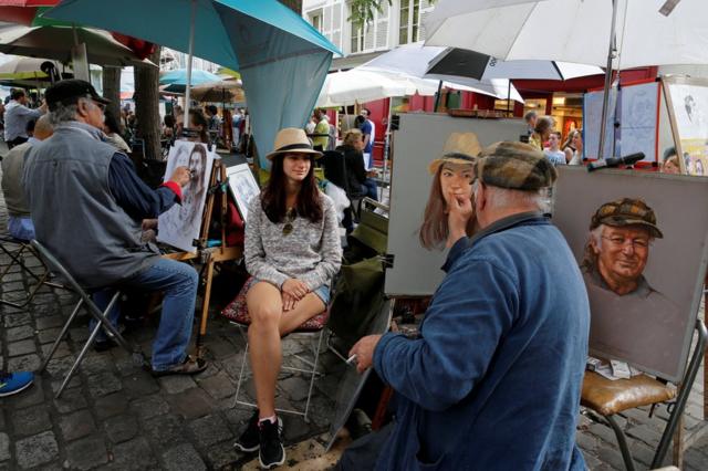 Un artista pinta un retrato de una joven turista cerca de la iglesia del Sagrado Corazón en Montmartre, París.