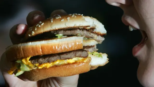 Imagem mostra mulher comendo pão com hamburguer