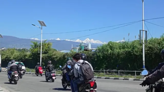 हिमाल र पहाडहरूको शृङ्खला देखिने काठमाण्डूको एउटा सडकमा गुडिरहेका मोटरसाइकल र स्कूटरहरू