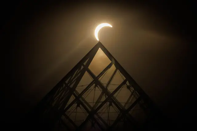 La luna pasa sobre el horizonte del sol detrás de la Pirámide del Louvre, en París, Francia.