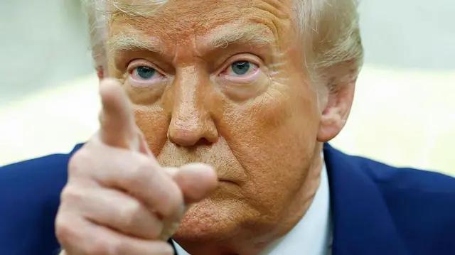 Лицо Дональда Трампа крупным планом, в кадре также видно его палец, указывающий в аудиторию