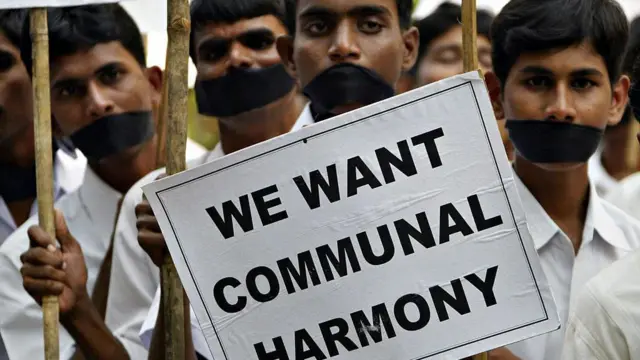 मुंह पर पट्टी बांधे खड़े युवा