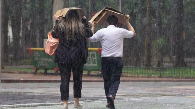 Pessoas correndo da chuva com papelão na cabeça