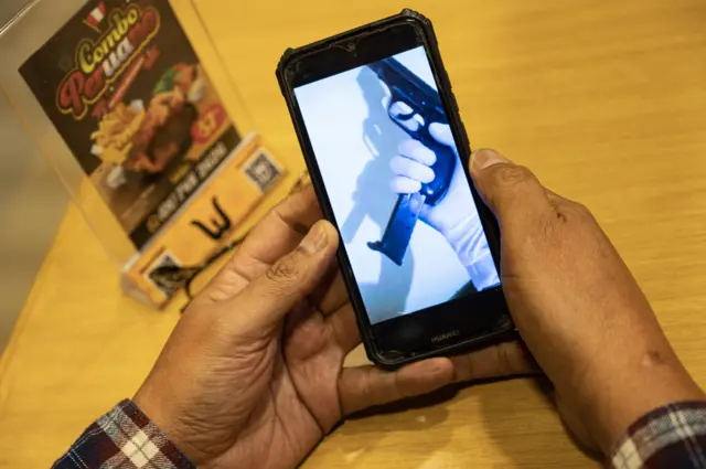 Un hombre muestra en su teléfono el video en el que lo amenazan.