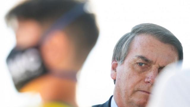 Bolsonaro olha para o lado, perto de apoiador com máscara de prevenção ao coronavírus