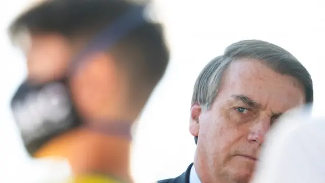 Bolsonaro olha para o lado, perto1xbet filmes onlineapoiador com máscara1xbet filmes onlineprevenção ao coronavírus