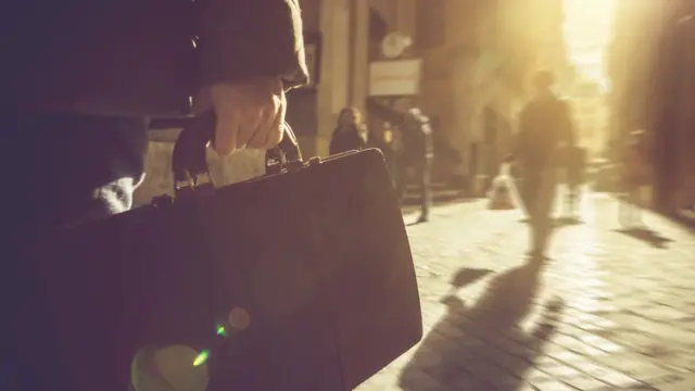 Homem caminha pela rua segurando uma pasta