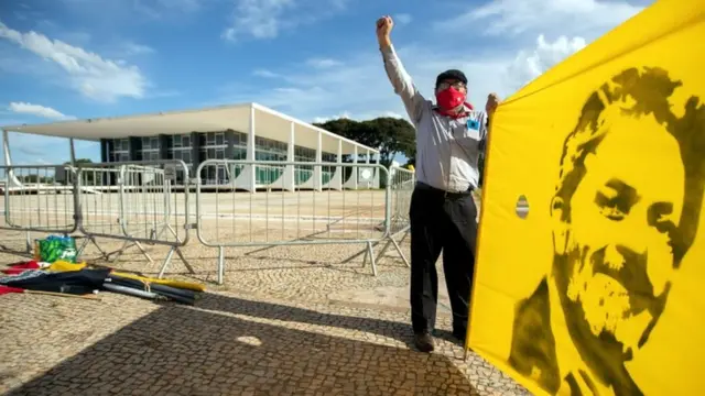 Homemjogos galera betfrente ao STF com braço erguido e, com a outra mão, segurando bandeira com desenhojogos galera betLula