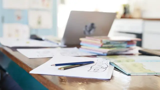 Material escolar sobre mesa com computador ao fundo