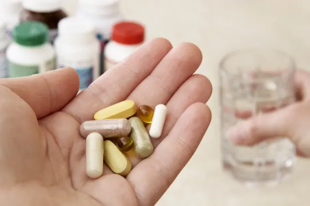 Una persona sostiene en sus manos varias vitaminas
