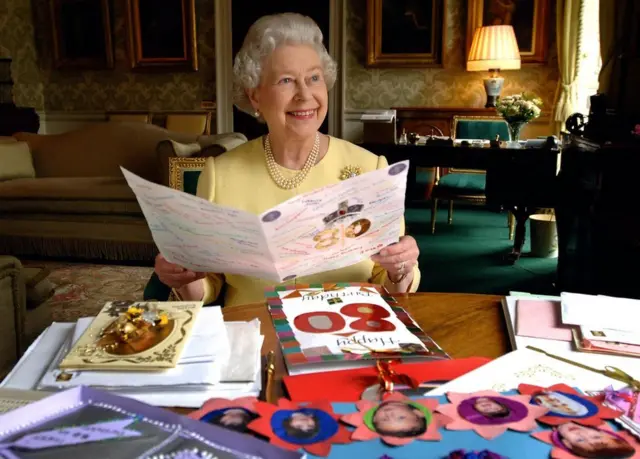 La reina Isabel II sentada en la Sala Regency del Palacio de Buckingham en Londres mientras mira algunas de las tarjetas que le han enviado por su cumpleaños 80.