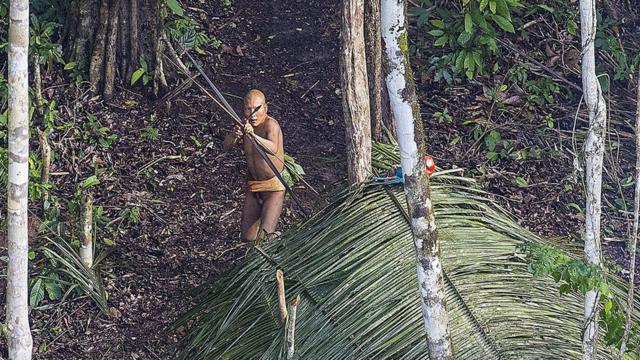 Indígena isolado no estado do Acre aponta uma flecha para o helicóptero acima de sua aldeia