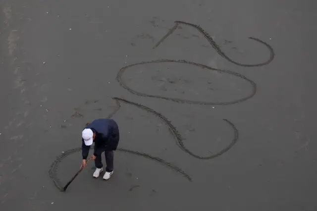 নিউজিল্যান্ডের ক্রাইস্টচার্চে বালির ওপর ২০২০ লিখছেন একজন শিল্পী
