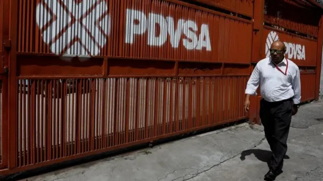 Un hombre camina al lado de un mural que lleva pintado el logo y nombre de "PDVSA"