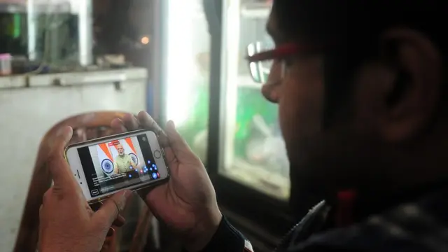 आदमी मोबाइल पर मोदी का भाषण सुनते हुए