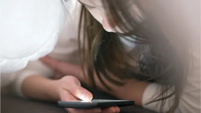 Дівчинка дивиться на екран смартфону вночі