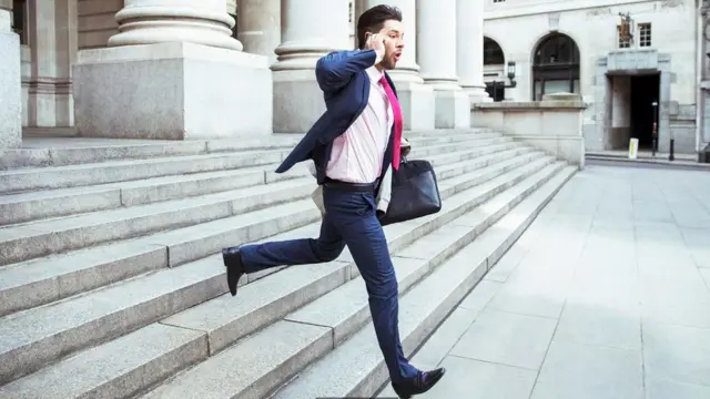 Un hombre corriendo escaleras abajo, mientras habla por un celular