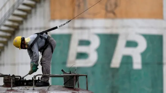 Operário agachado e trabalhandounibets 365frente a logo da Petrobras pintado no muro