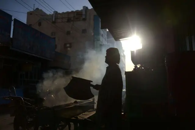 Homem na contraluz abana churrasco na rua