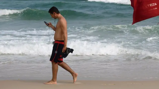 Homem na praia com celular