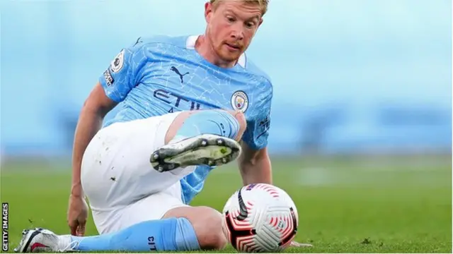 Kevin De Bruyne controls the ball while sat on the pitch