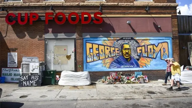 Flores e grafite com retrato de Floyd em frente a loja de conveniência, em foto diurna