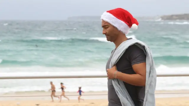 د اسټرالیا سیډني ته نږدې سمندرغاړه کې یو کس چې سنټا خولۍ یې پر سر ده. نیمه لوېدیځه کوره کې اوس دوبي او هوا مناسبه ده.