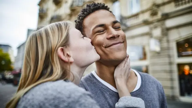 Un jeune couple semble heureux, alors que la femme embrasse l'homme sur la joue