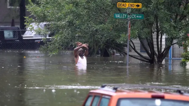 مردی که در سیل گرفتار شده دستش را برای نیروهای امداد تکان می‌دهد