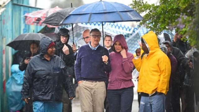 Bill and Melinda Gates brace the rain as they visit the township of Khayelitsha on October 25, 2019 in Cape Town, South Africa
