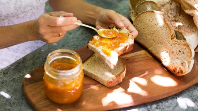 Una persona sirve mermelada sobre un pan.