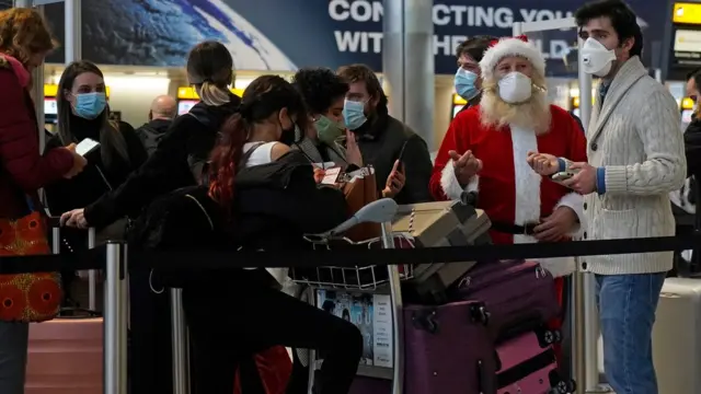 Des voyageurs masqués, dont un déguisé en Père Noël, font la queue dans le hall des départs de l'aéroport d'Heathrow à Londres.