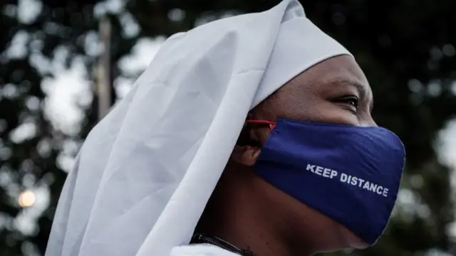 Une adoratrice de Legio Maria porte un masque de protection portant l'inscription "Gardez vos distances" lorsqu'elle arrive pour assister à une prière à leur église dans le bidonville de Kibera à Nairobi, le 26 juillet 2020, après que le président du Kenya ait autorisé la réouverture des lieux de culte selon des directives strictes pour freiner la propagation du nouveau coronavirus (COVID-19).