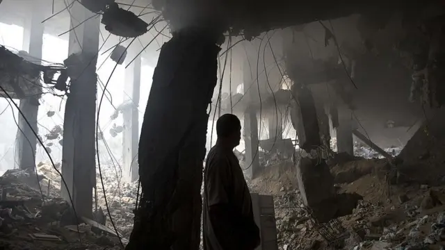 رجل فلسطيني يتفقد أنقاض متجر مدمر في مبنى أصيب بغارة جوية إسرائيلية، مدينة غزة