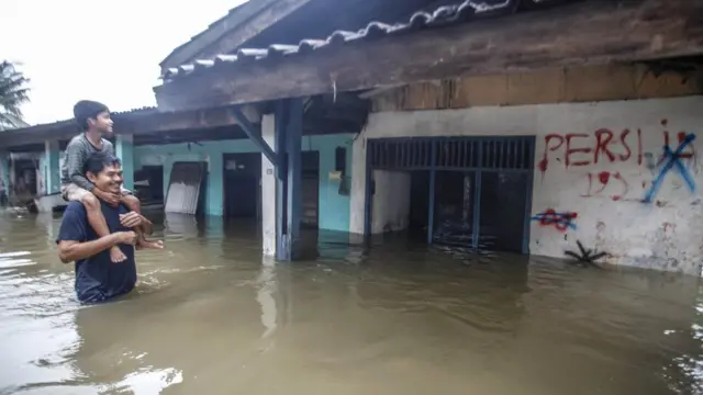 Warga melintas di depan rumah yang terendam banjir di kawasan Cilangkap, Jakarta Timur, Selasa (25/02).
