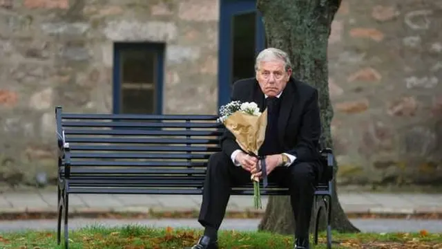 Homem com buquê de flores assiste ao cortejo da rainha