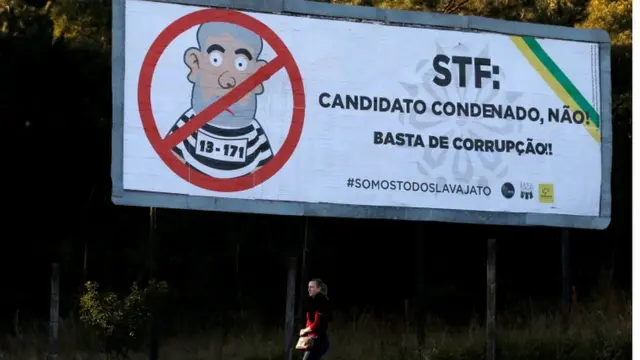 Mulher passa por outdoor com ilustraçãojogos de bolhas grátisLula vestidojogos de bolhas grátispresidiário e mensagem ao STF 'Candidato condenado não'