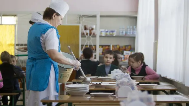 Повариха в столовой насыпает детям суп