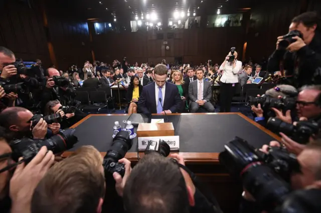 Mark Zuckerberg sits in front of photographers